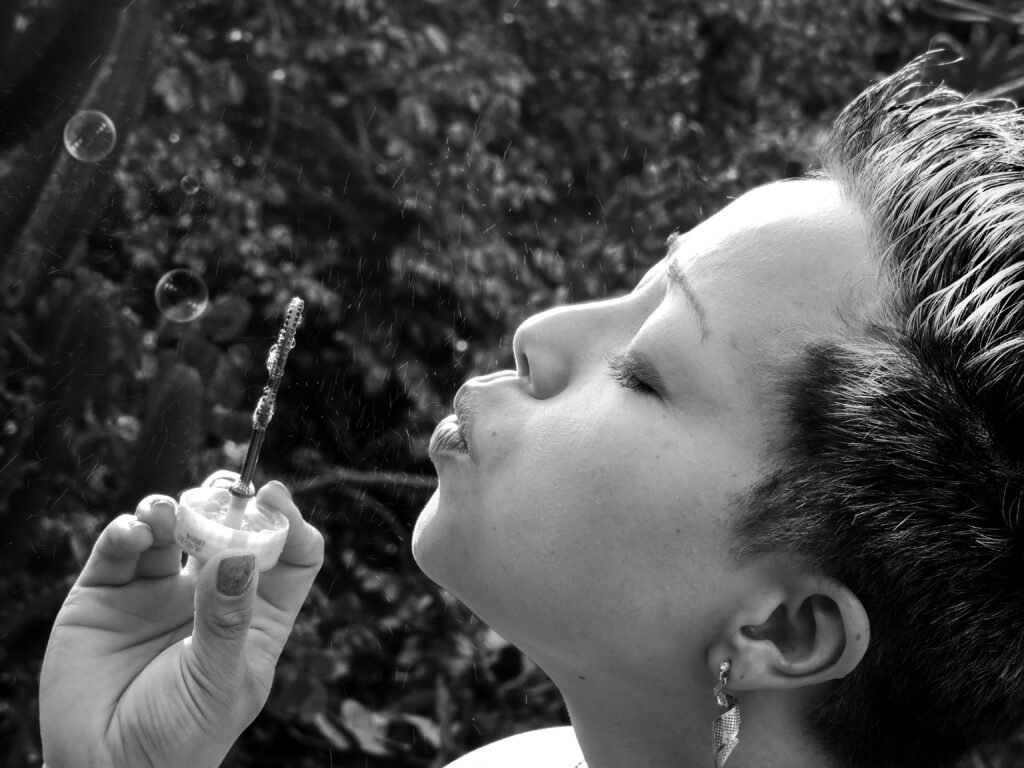 Retrato artístico em preto e branco de Paula Ratsue Siguematsu, diretora de arte da Agência Sue, soprando bolhas de sabão em um momento de criatividade ao ar livre.